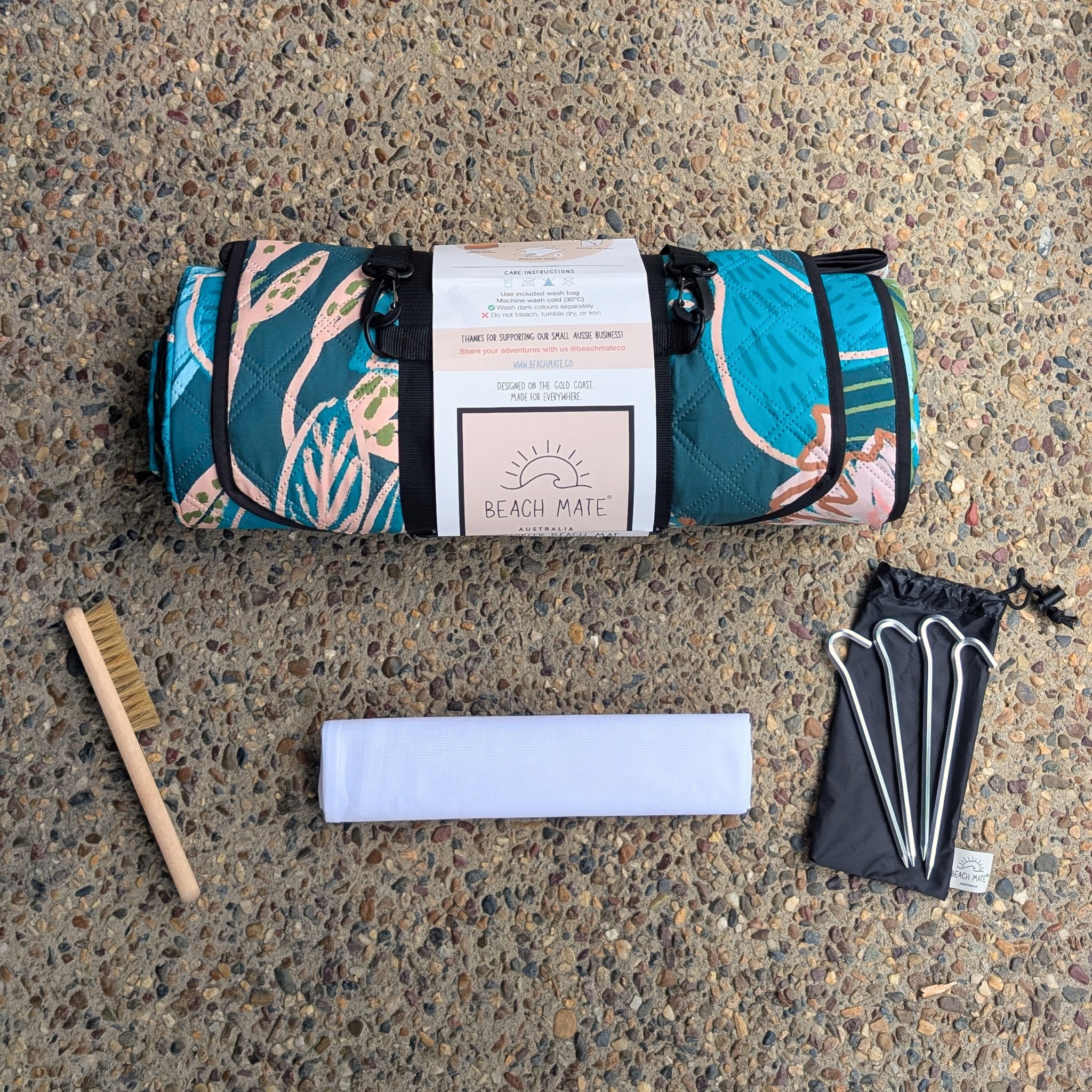 Flatlay of the Talle Valley Beach Mate with inclusions — brush, wash bag, and aluminium pegs.