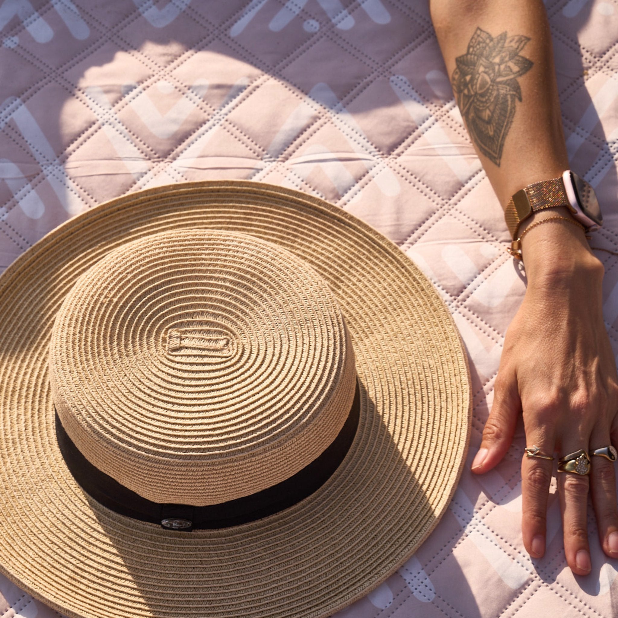 Beach Mate Palm Beach sand-free recycled beach mat close-up with straw hat and tattooed arm resting on mat